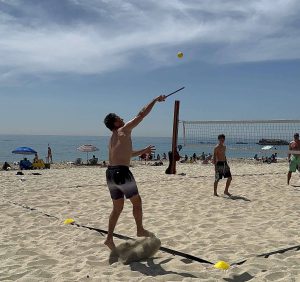 Sandy Pickle player serving a pickleball on a beach volleyball court